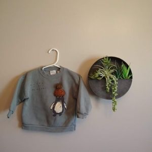 Zara dusty green/blue sweatshirt with penguin and says "enjoy the moment"